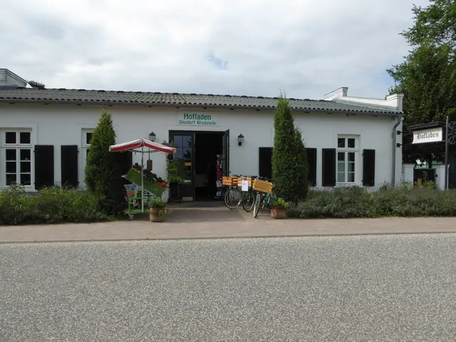 Bâtiment blanc de la ferme abritant sa boutique, cyprès et vélos devant l'entrée