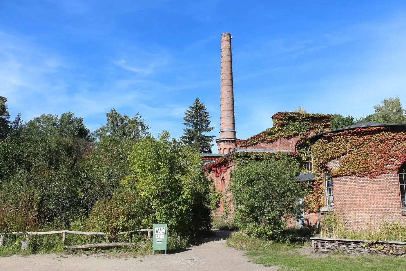 Bâtiment de brique de l'ancienne station de pompage et sa haute cheminée, au milieu des arbres