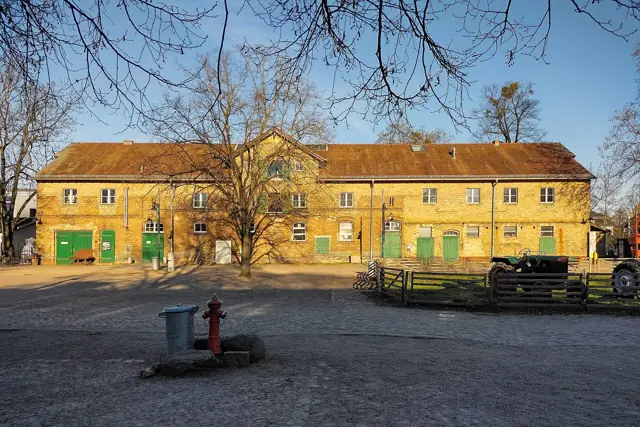 Cour de la ferme-musée entourée de longs bâtiments agricoles jaunes
