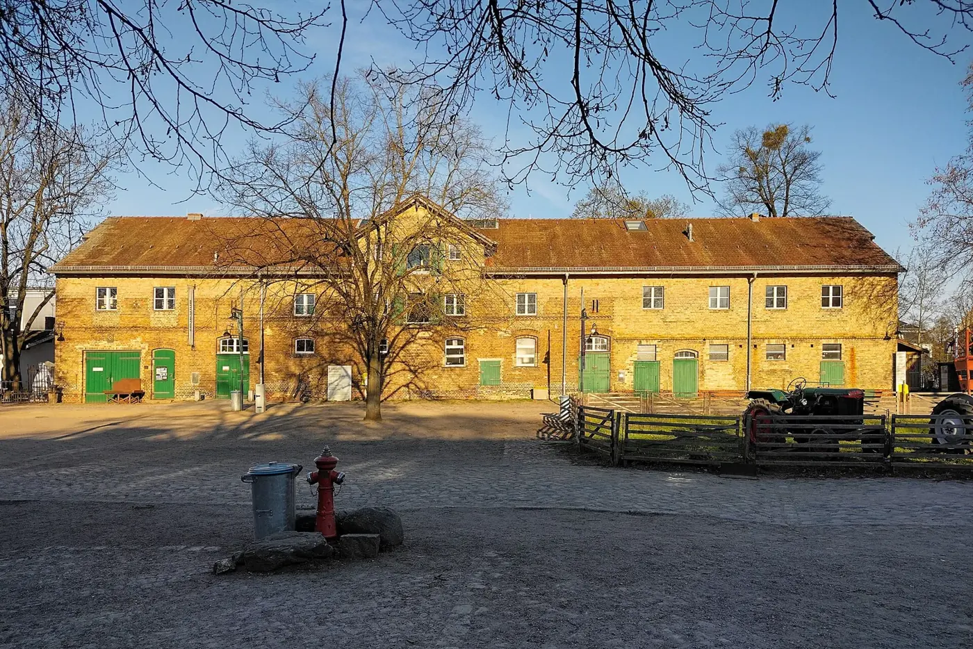 Cour de la ferme-musée entourée de longs bâtiments agricoles jaunes