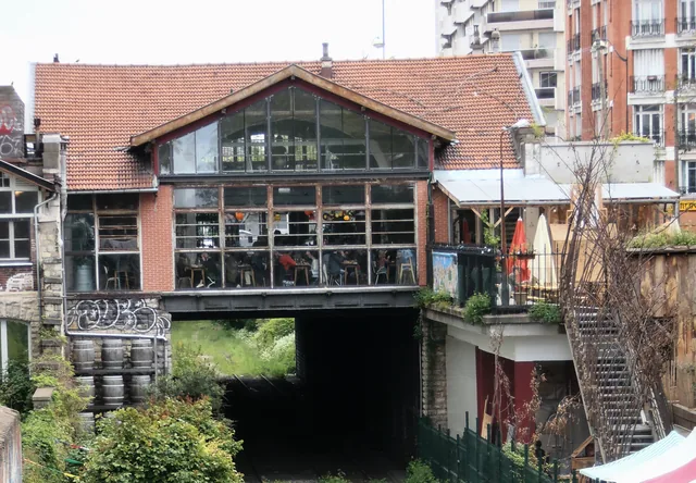Ancienne gare de la Petite Ceinture réhabilitée, ses voies envahies par la végétation et la ferme urbaine sur le talus