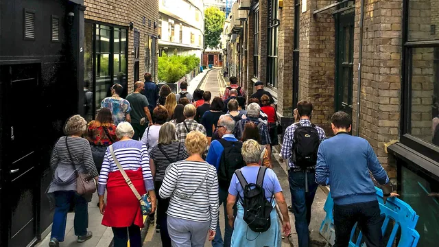 Groupe de visiteurs de dos suivant leur guide dans une ruelle de brique londonienne