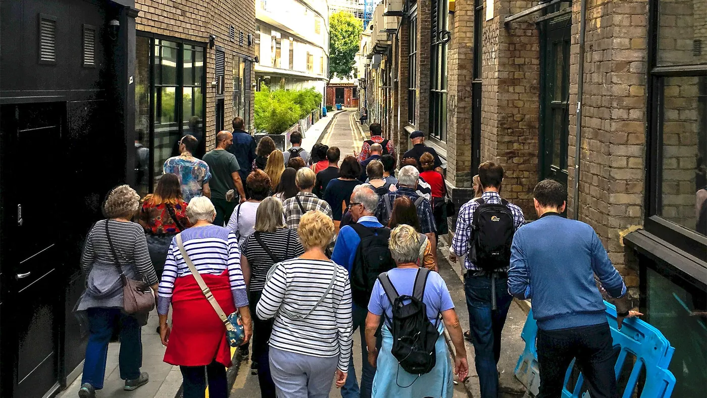 Groupe de visiteurs de dos suivant leur guide dans une ruelle de brique londonienne