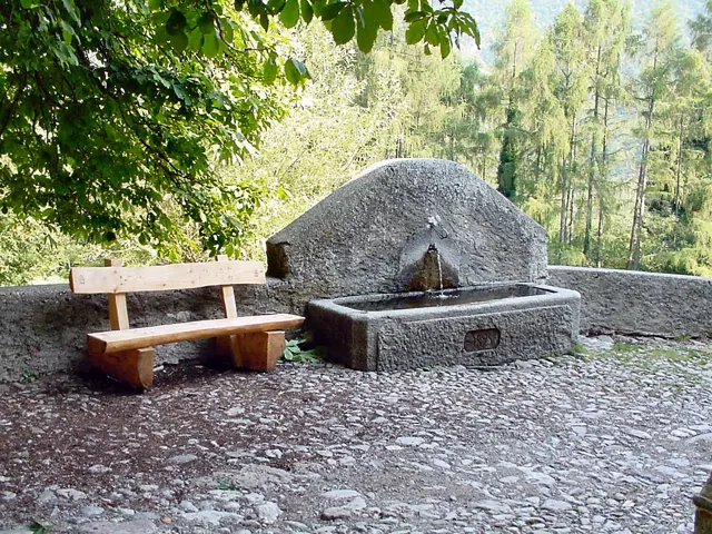 Voyage scolaire durable à Milan : fontaine de pierre et banc de bois dans une clairière des Préalpes